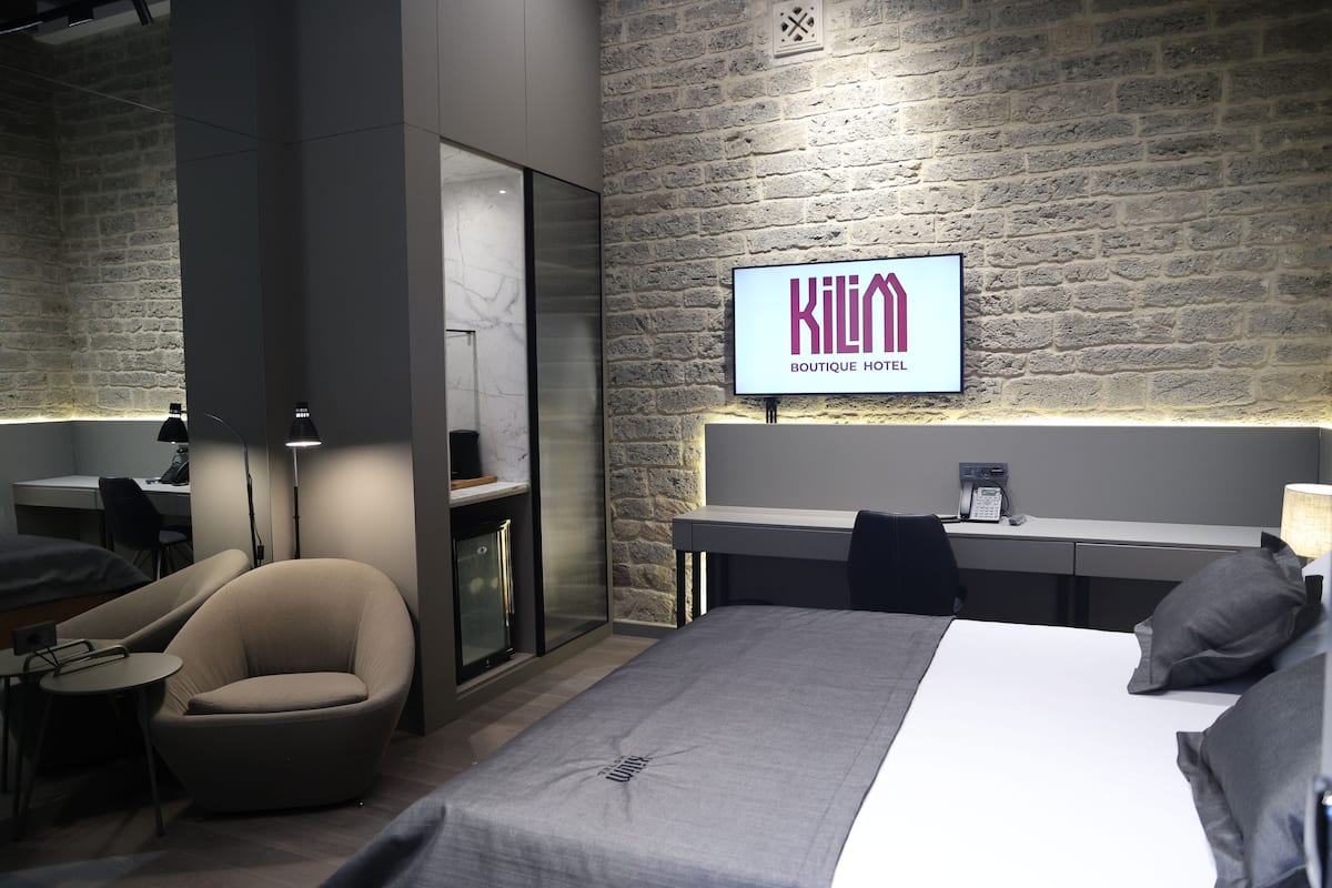 Ein modernes Hotelzimmer mit einem Bett, einem Schreibtisch, einem Stuhl und einem Fernseher, der den Namen des Hotels zeigt.