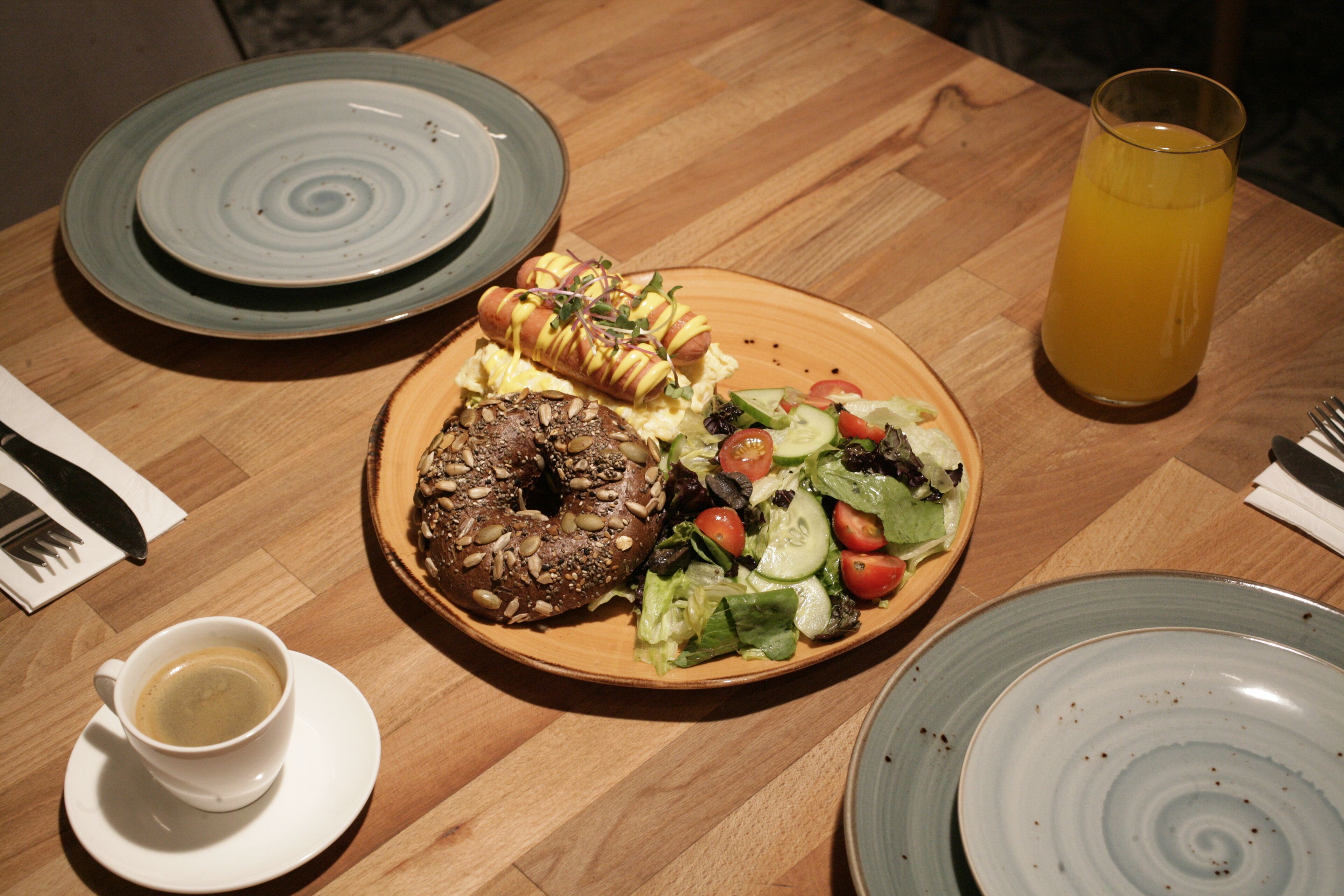 A wooden table with a plate of food, a glass of orange juice, and a cup of coffee.