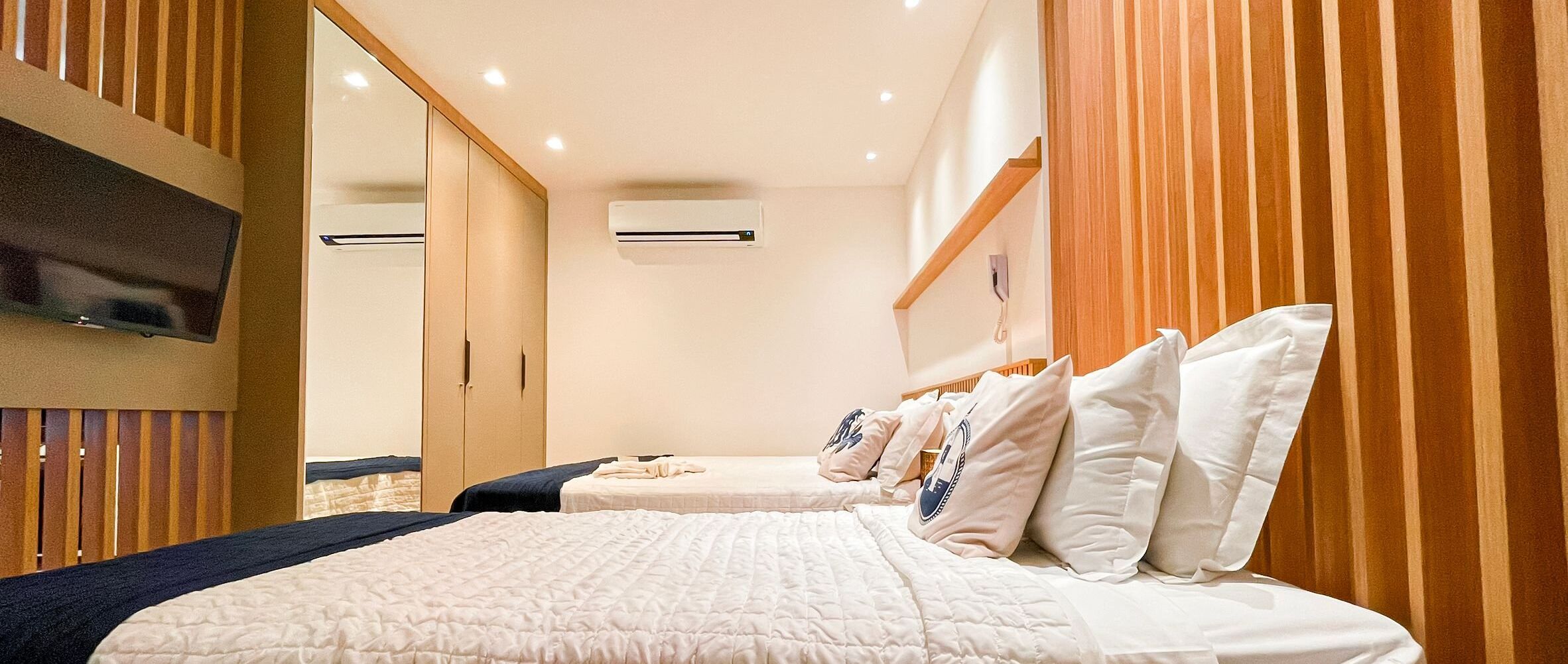 Habitación de hotel con una cama grande, televisor montado en la pared y cabecero de madera.