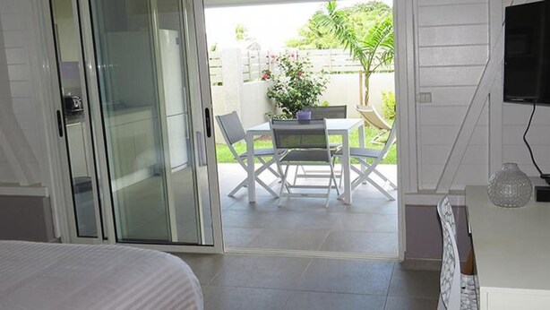 Ein Schlafzimmer mit einem Bett, einer Glasschiebetür, die auf eine Terrasse mit Tisch und Stühlen führt, und einem an der Wand befestigten Fernseher.