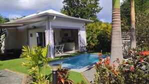 Ein Haus mit überdachter Terrasse, Pool und üppiger Bepflanzung.