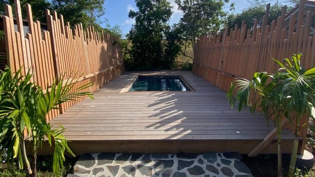 A wooden deck leading to a swimming pool with a stone border, surrounded by a wooden fence and greenery. - Ecolodge Barbuda - Natural Pool & Beach (Saint-François)