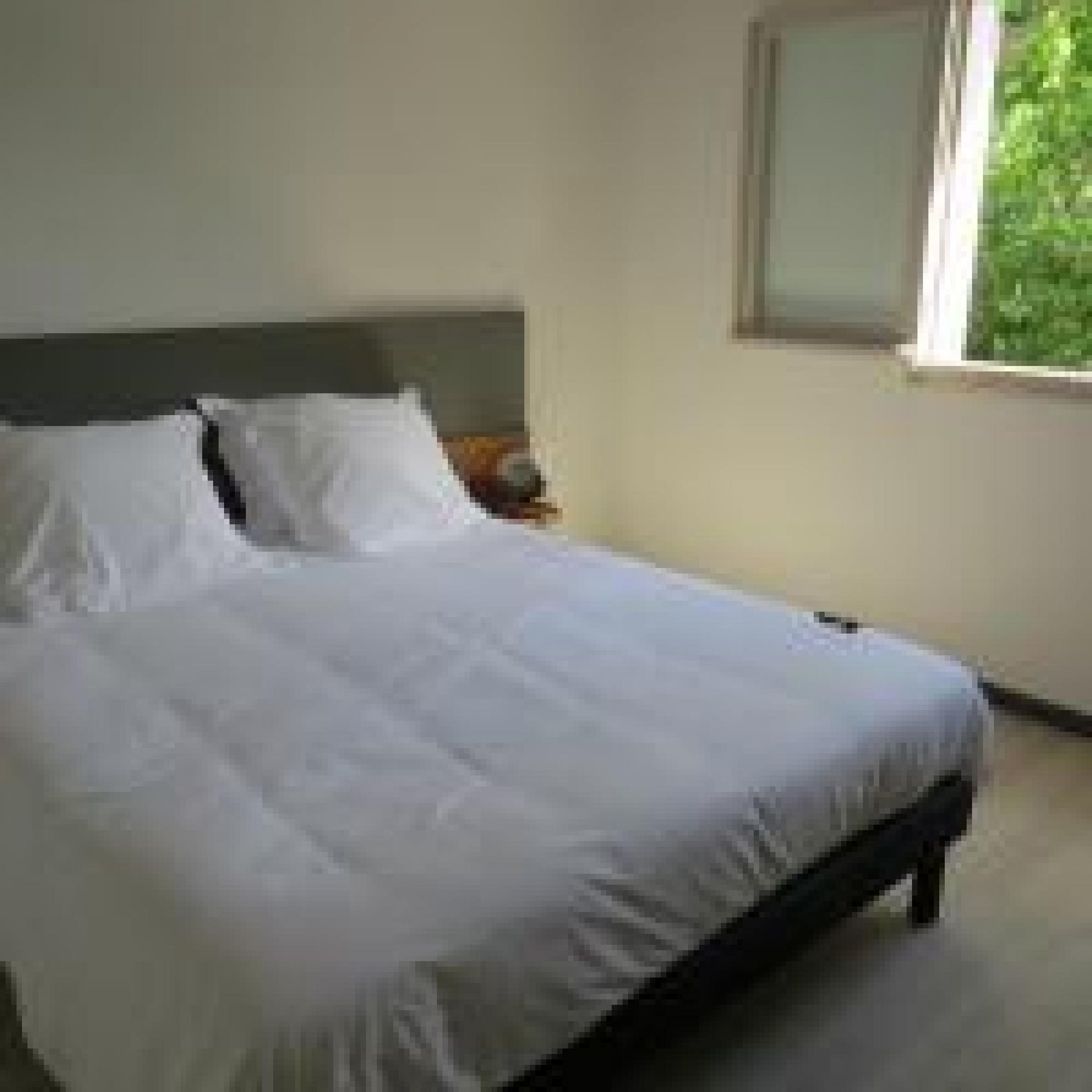 A neatly made bed in a room with a window and a nightstand.