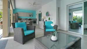 A modern living area with wicker furniture, a glass coffee table, and a view of the kitchen and outdoor space. - Villa the Lodge - Lagon Saint-françois (Saint-François)
