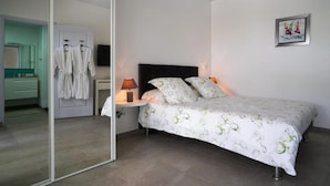 A bedroom with a bed, bedside table, and a mirror. There is a door leading to a bathroom. - Villa the Lodge - Lagon Saint-françois (Saint-François)