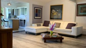 A modern living room with a sofa set, a coffee table, and a dining area with a kitchen in the background. - Villa Clara (Le Gosier)