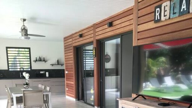 A modern living room with a wooden cabinet, a flat-screen TV, and a dining area with chairs and a table. - Villa Ambre (Saint-François)