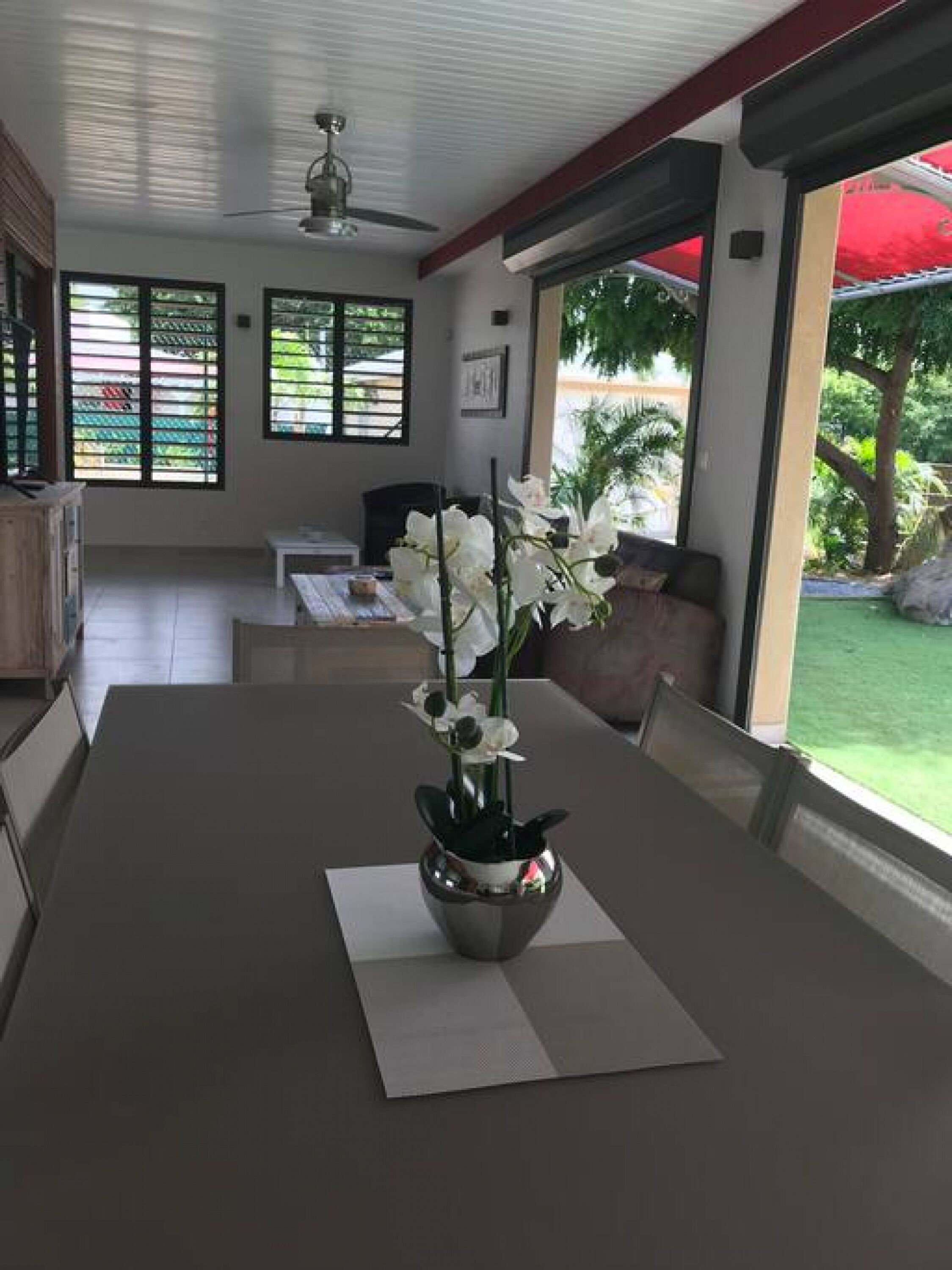 Un comedor moderno con una mesa dispuesta para dos, un jarrón de orquídeas blancas y vistas a un jardín exuberante a través de grandes ventanales.