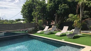 A swimming pool with clear water, surrounded by artificial grass and white lounge chairs. - Villa Ambre (Saint-François)