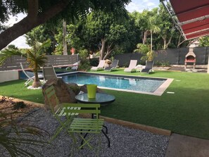 En trädgård med en pool, konstgräs, solstolar och en grillplats.