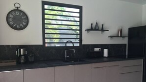 A modern kitchen with a black countertop, a sink, a coffee maker, and a window with blinds. - Villa Ambre (Saint-François)
