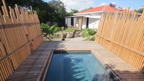 A rectangular hot tub surrounded by wooden decking, with a wooden fence on one side and a house in the background. - Ecolodge Saba - Natural Pool & Beach (Saint-François)