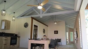 A spacious kitchen with wooden cabinets, a dining table, and chairs. There is a ceiling fan, pendant lights, and a clock on the wall. - Ecolodge Saba - Natural Pool & Beach (Saint-François)