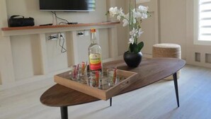 A modern living room with a wooden coffee table, a bottle of liquor, and a vase of white flowers. - Ecolodge Anguila - Natural Pool & Beach (Saint-François)