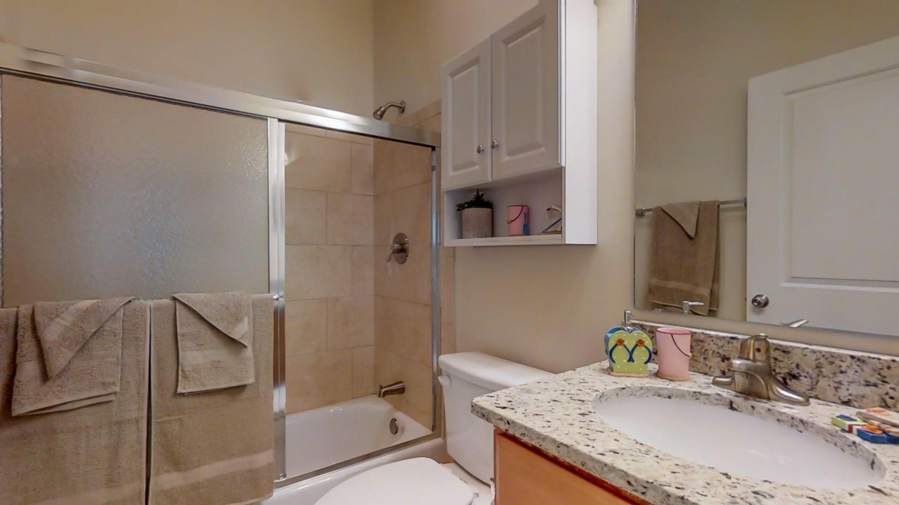A bathroom with a shower, toilet, sink, and a mirror.