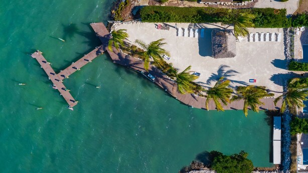 An aerial view of a coastal property with a pier extending into the water, a sandy beach area with palm trees, and a small pool. - 5 Beautiful 4 Bed 3 Bath Pool Home w Free Dock (Marathon)