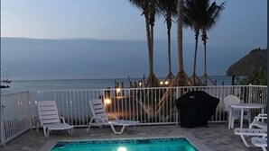 Une piscine avec des chaises longues et une vue sur la mer au crépuscule.