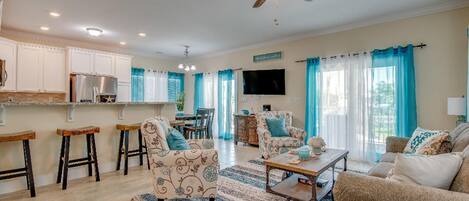A spacious living area with a kitchen, bar stools, a dining table, and a TV.