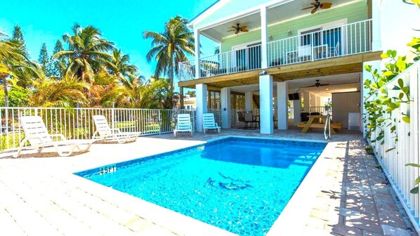 A pool area with a clear blue pool, white lounge chairs, and a covered seating area with a ceiling fan. - 8 Waterfront 4 Bed 3 Bath Pool Home w Free Dock (Marathon)
