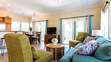 A living room with a sofa, chairs, a coffee table, a TV, and a balcony with curtains.