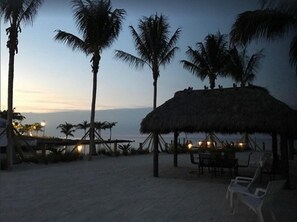 A beach scene with palm trees, a thatched-roof hut, and beach chairs.