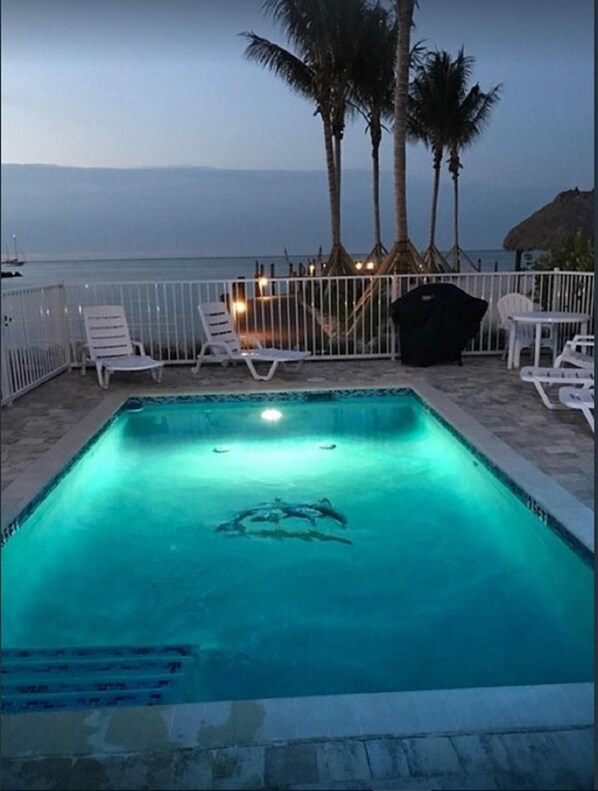 Une piscine avec des chaises longues et une vue sur la mer au crépuscule.
