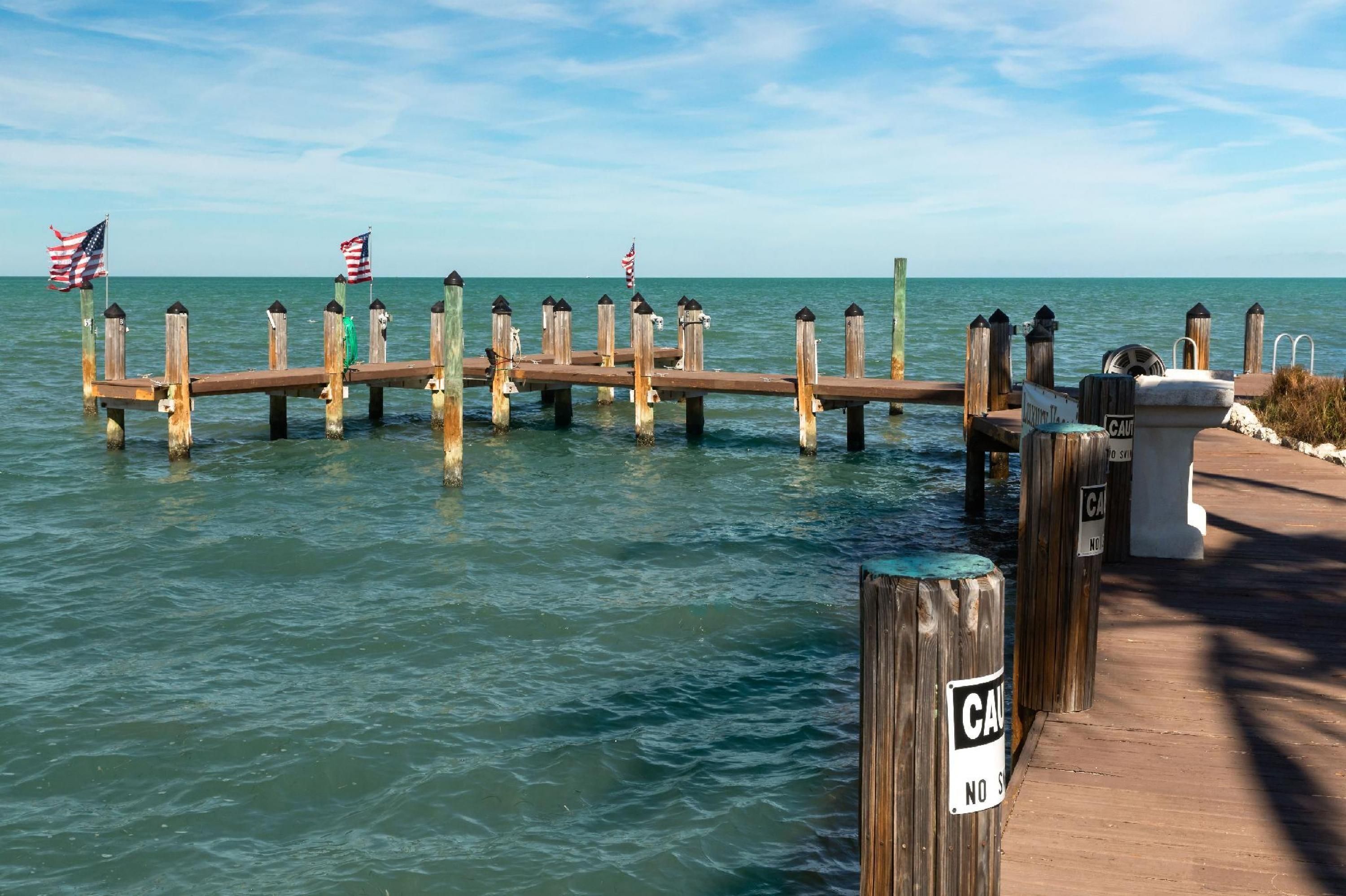 A wooden pier extending into calm waters with American flags and a 'No Swimming' sign.