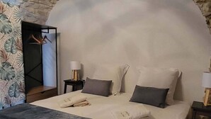 Un dormitorio con techo de piedra, una cama grande con colcha gris y blanca, una mesita de noche con lámpara y una pared con diseño de hojas.