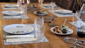 Una larga mesa de madera dispuesta para una comida, con platos, vasos y cubiertos.