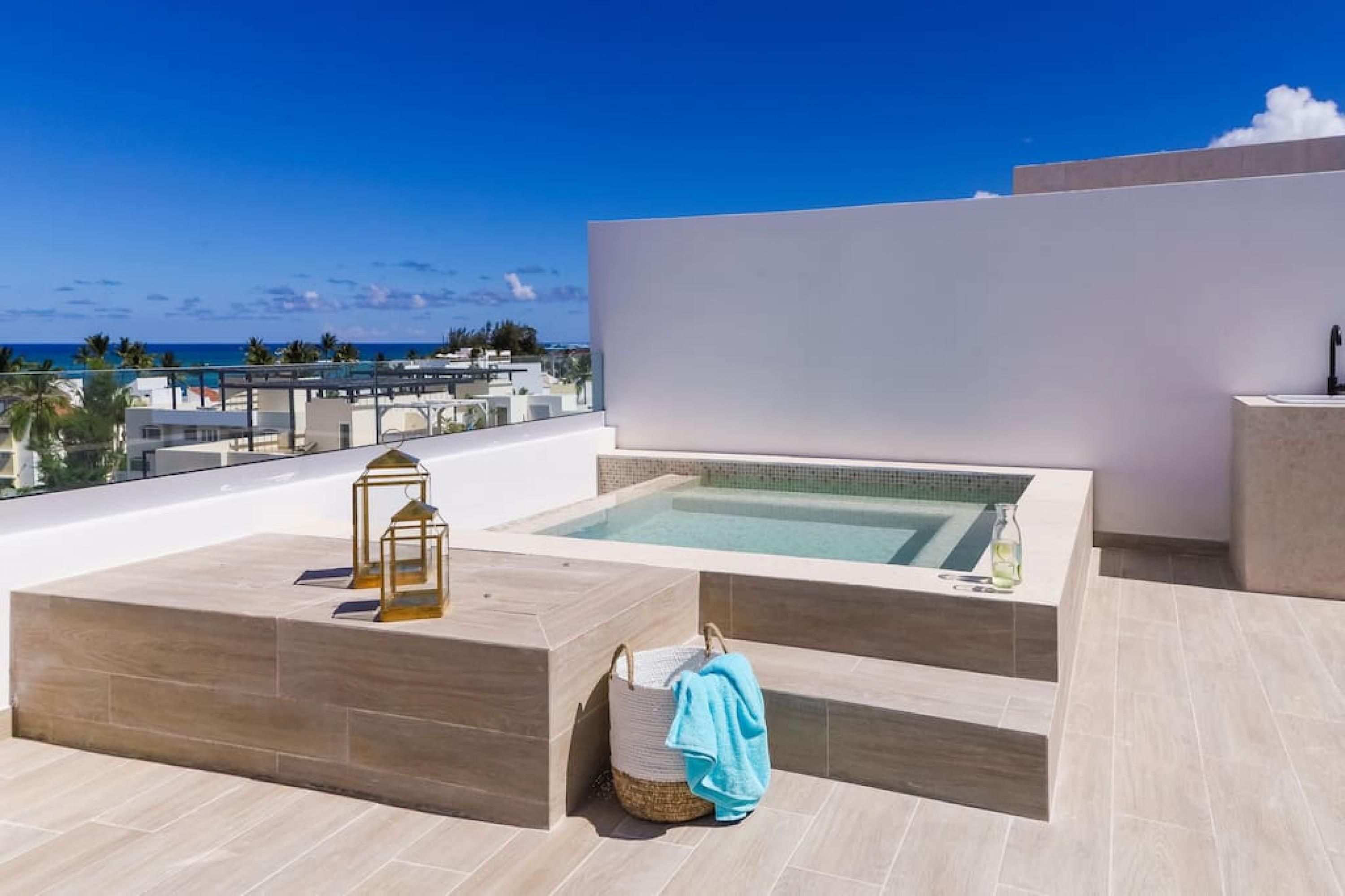 Une piscine sur le toit offrant une vue dégagée sur l’océan, un petit coin salon et une serviette posée sur le sol.
