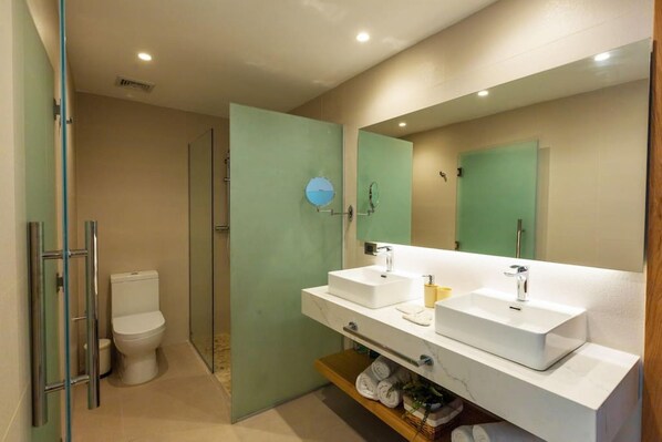 Un baño moderno con un lavamanos blanco, un espejo grande y una cabina de ducha de vidrio.