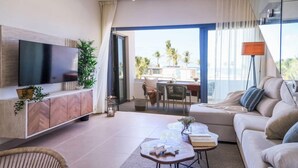 Un salon moderne doté d’un téléviseur à écran plat, d’un canapé, d’un coin repas et d’un balcon offrant une vue sur les palmiers.