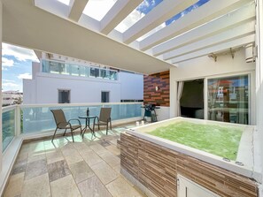Un balcón con una mesa y sillas de vidrio, un jacuzzi y vistas de un edificio moderno.
