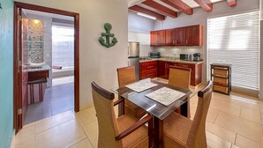 A compact kitchen with wooden cabinets, a built-in microwave, and a glass dining table with wicker chairs. - Gorgeous 1 BR PH Apartment w Jacuzzi (Punta Cana)