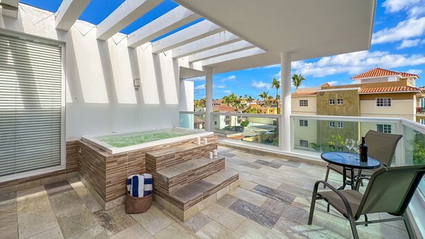 A balcony with a hot tub, a table with chairs, and a view of neighboring buildings. - Gorgeous 1 BR PH Apartment w Jacuzzi (Punta Cana)