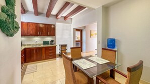 A modern kitchen with wooden cabinets, a dining area with wicker chairs, and a water dispenser. - Gorgeous 1 BR PH Apartment w Jacuzzi (Punta Cana)