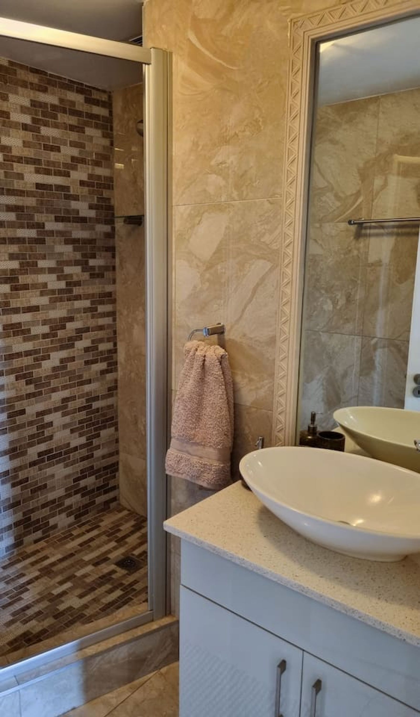 Un baño con pared de ducha azulejada, un lavabo color beige y un espejo con marco decorativo.