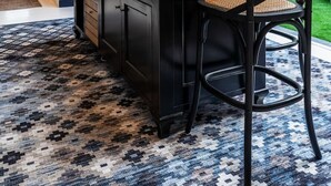 Une cuisine moderne dotée d’un îlot central, de meubles de couleur sombre et d’un tapis à motifs.