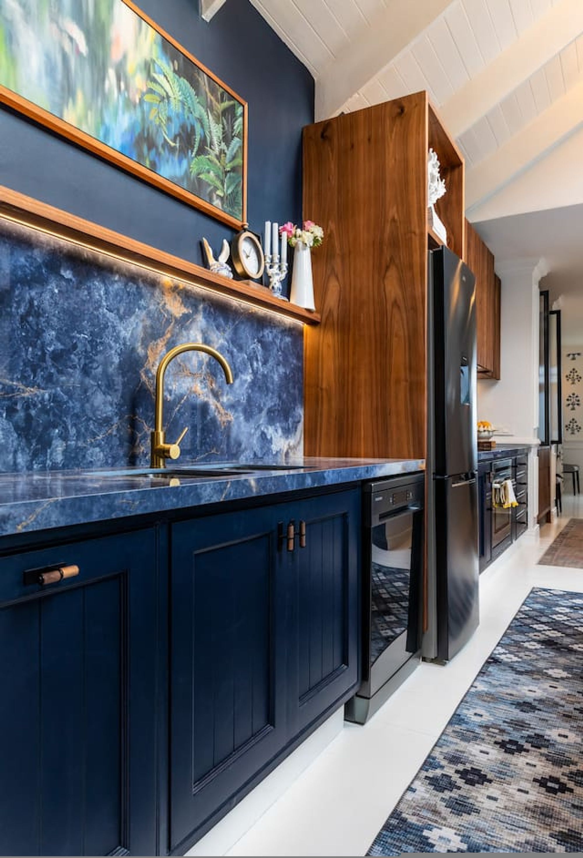Una cucina moderna con mobili scuri color blu, un piano di lavoro in marmo e una parete d'accento in legno.
