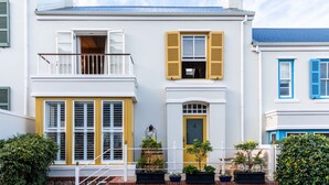 Un immeuble de deux étages doté d’un balcon, d’une porte jaune et de plantes en pot disposées sur les marches de l’entrée.