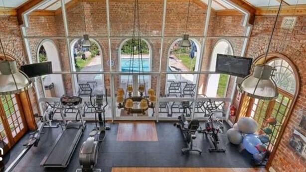 Un gimnasio con equipo de ejercicio, ventanas amplias y vista a una piscina.