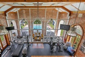 A gym with exercise equipment, large windows, and a view of a swimming pool. - Charming Coastal Townhouse at The Majestic (Cape Town)