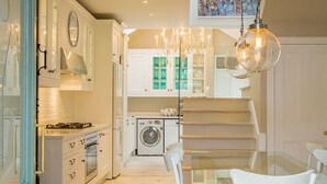 Una cocina moderna con armarios blancos, una zona de comedor con mesa de vidrio y sillas blancas, y un tapete colorido.