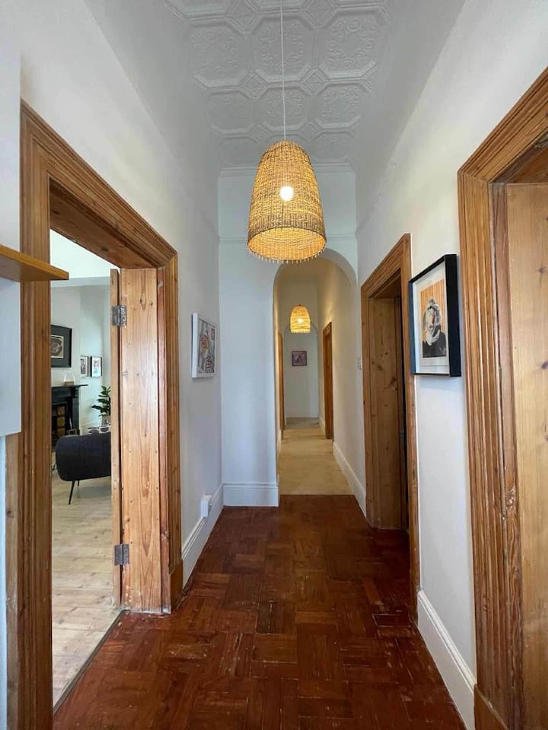 A hallway with wooden doors, a woven ceiling light fixture, and a carpeted floor.