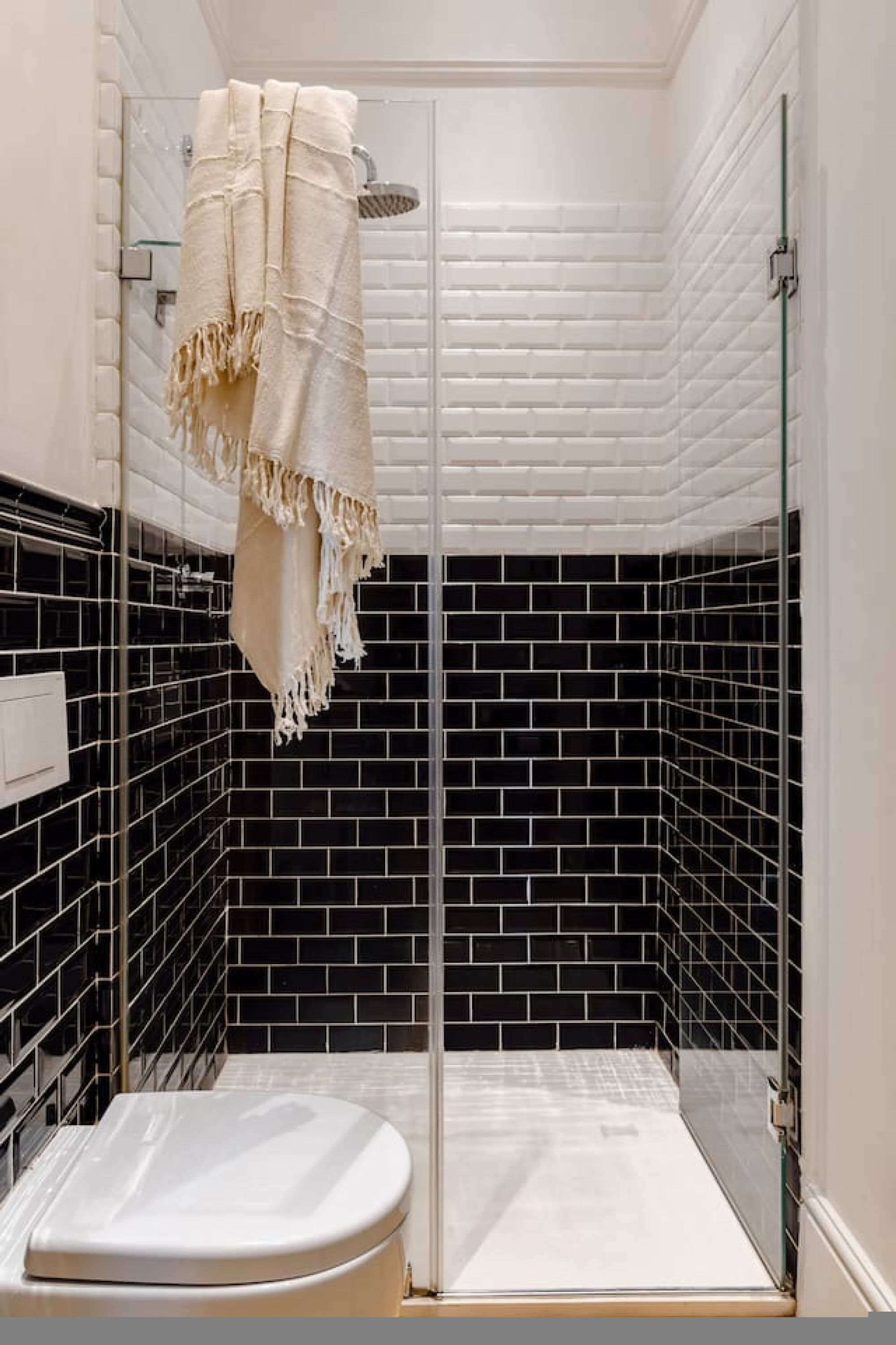 A bathroom with a glass shower enclosure, black and white tiled walls, and a white toilet.