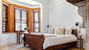 A bedroom with a wooden bed, a desk, and a window with wooden shutters. - FIR Villa 3 Bedroom House Greenpoint (Cape Town)