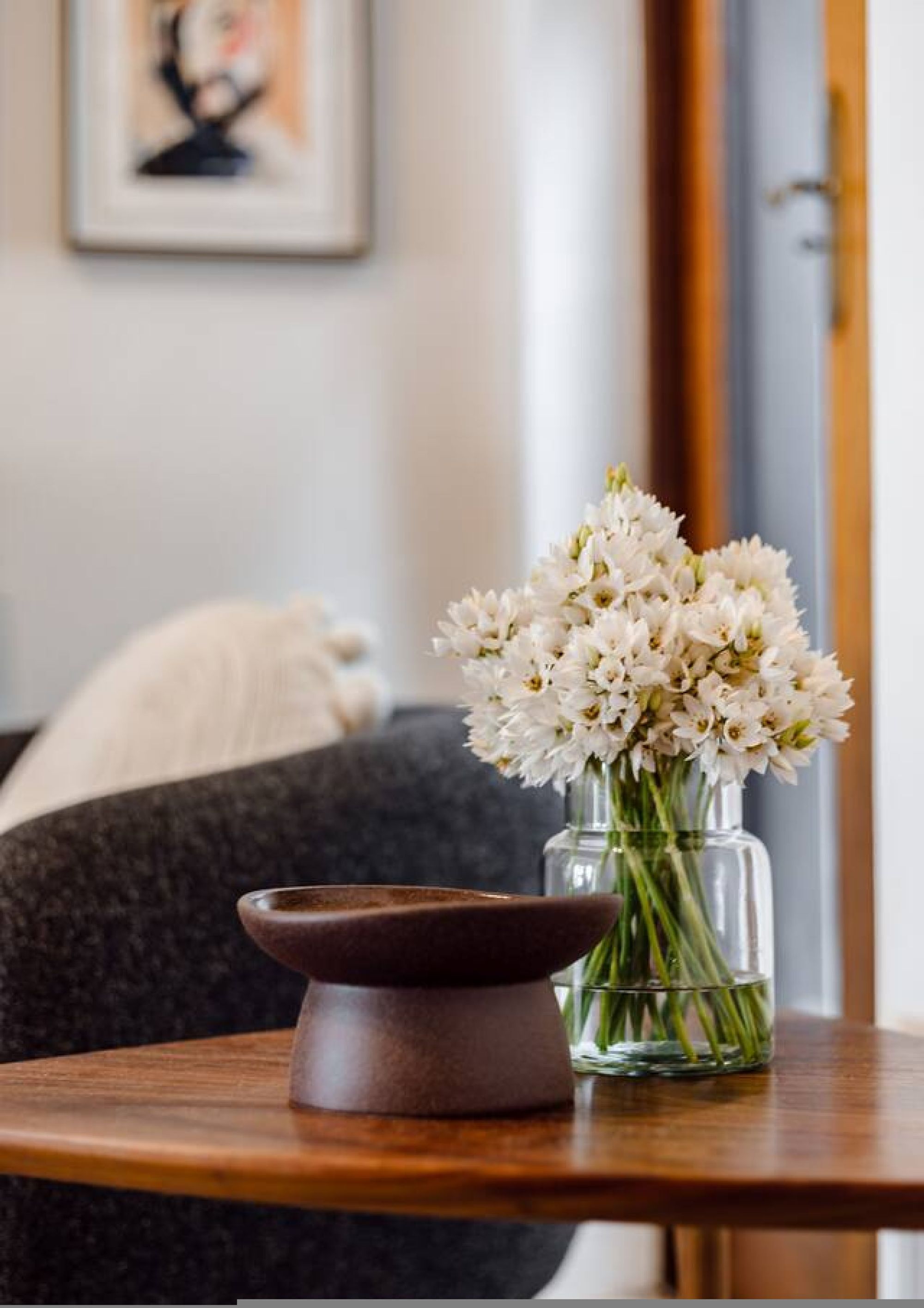 Een tafel met een vaas witte bloemen en een bruine schaal.