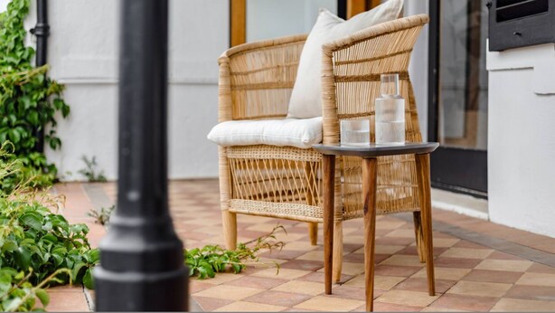 A wicker chair with cushions and a table with glasses on a tiled patio. - FIR Villa 3 Bedroom House Greenpoint (Cape Town)