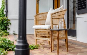 Een rieten stoel met kussens en een tafel met glazen op een betegeld terras.
