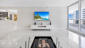 Un salon moderne avec un grand téléviseur à écran plat fixé au mur, un meuble de rangement blanc en dessous et un magazine posé sur une table basse.